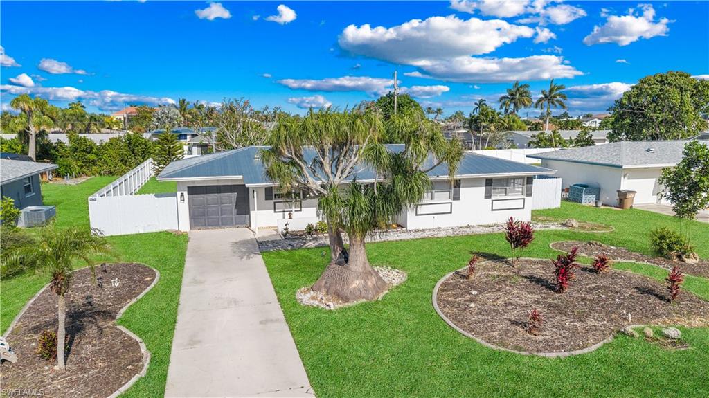 The property features a well-maintained front yard with a concrete driveway, established landscaping, and a fenced perimeter