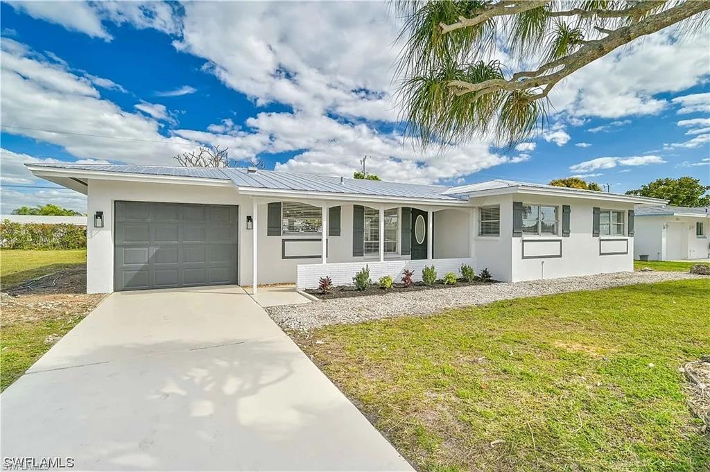 The property features a white exterior with a gray garage door, a driveway, and a well-maintained lawn