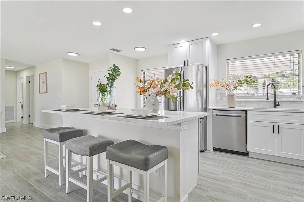 The kitchen features an island with seating, white cabinetry, stainless steel appliances, and large windows with blinds