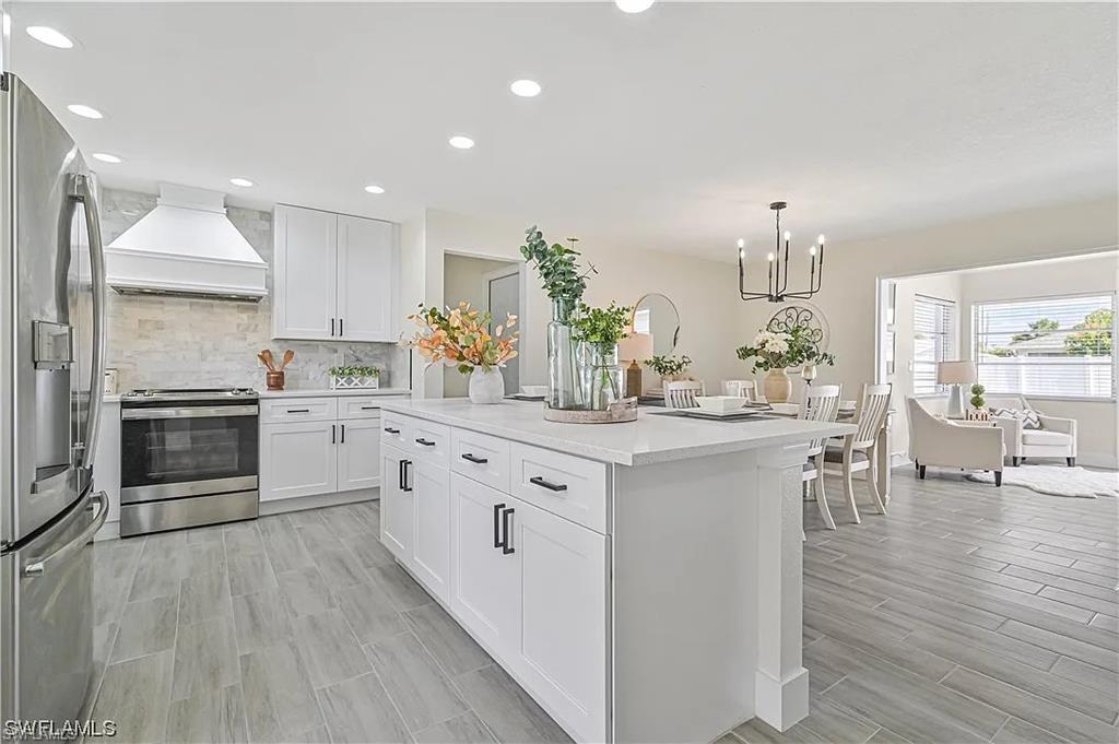 The kitchen features white cabinetry, stainless steel appliances, and a central island with a light-colored countertop, complemented by recessed lighting and light-toned flooring