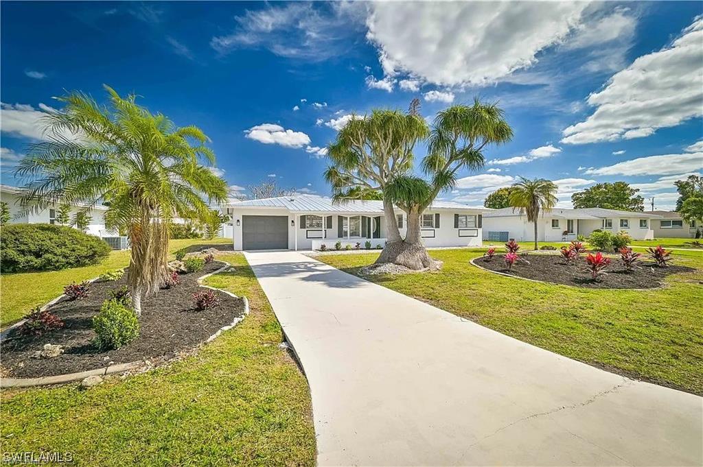 The property features a well-maintained lawn, a paved driveway, and established landscaping with palm trees