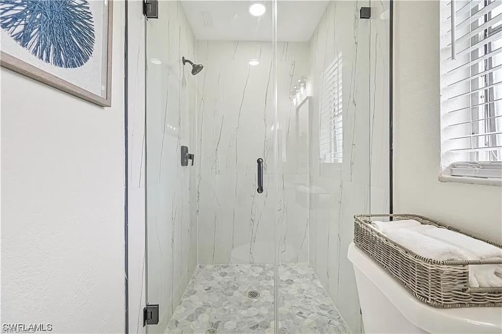 Shower with a clear glass enclosure, white marble-style wall tiles, and pebble-style floor tiles