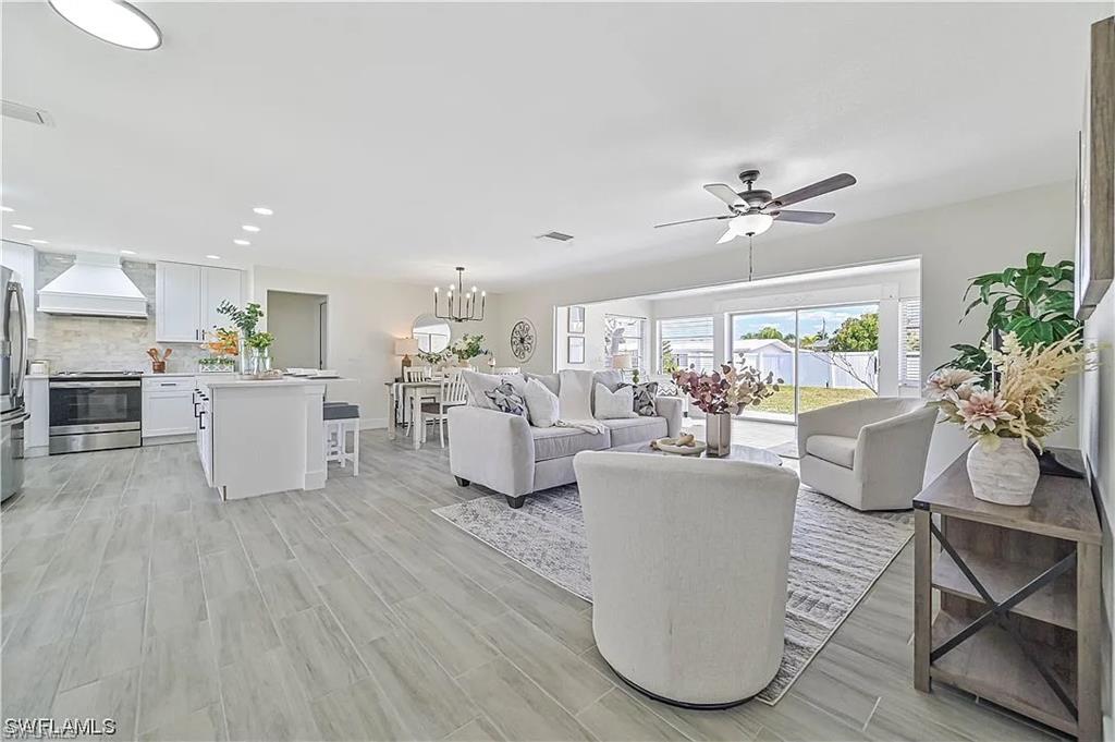 Open concept living area featuring light-toned flooring, a kitchen with white cabinetry and stainless steel appliances, and a living room with a ceiling fan