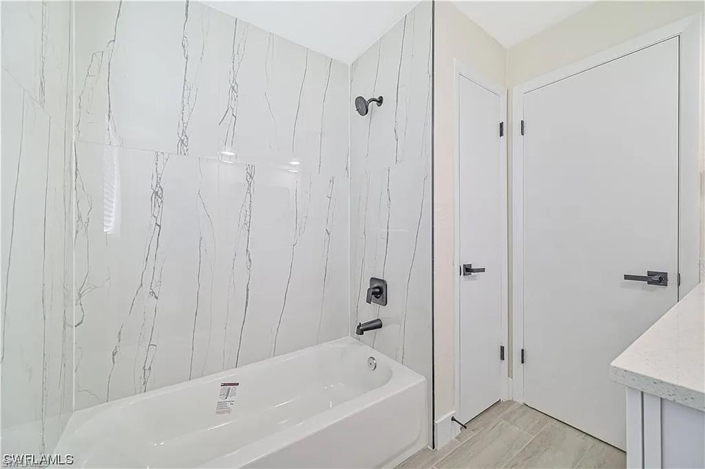Bathroom featuring a white bathtub, white marble-patterned shower tiling, and dark-toned fixtures
