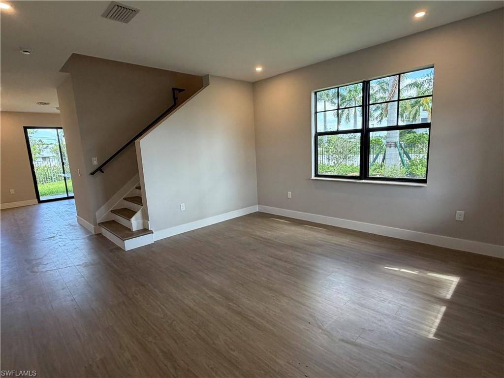 Spacious living area featuring light-toned flooring, recessed lighting, and a large window providing ample natural light and views of tropical foliage