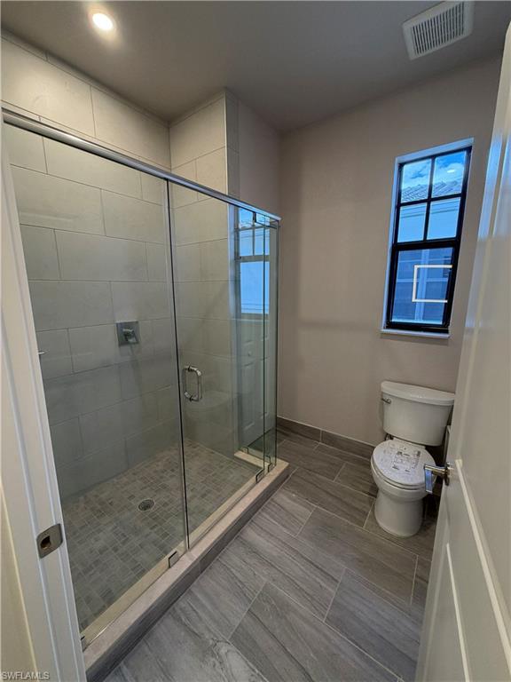 Bathroom featuring a glass-enclosed shower with tiled walls and floor, a toilet, and light-colored tiled flooring