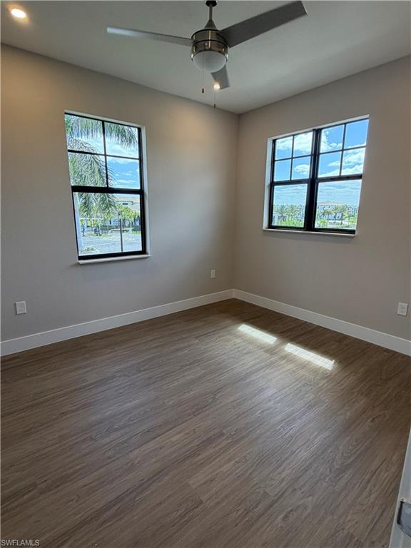 This room features durable plank flooring, two windows with views of the surrounding area, and a ceiling fan with integrated lighting