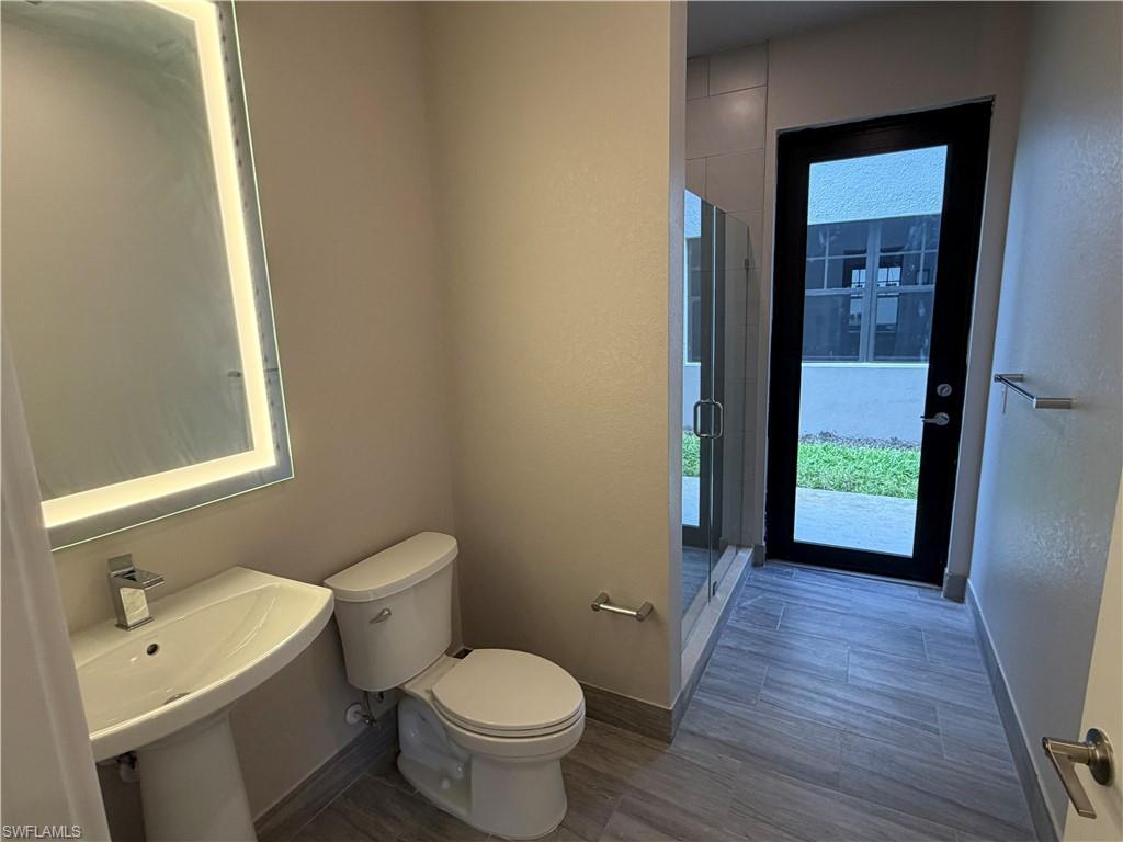Bathroom featuring a pedestal sink with a modern faucet, a toilet, an illuminated mirror, and a glass-enclosed shower