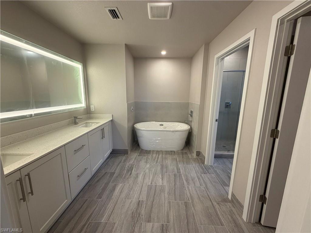 Bathroom featuring a dual vanity with light-colored countertops, an illuminated mirror, a freestanding soaking tub, and a separate shower with a glass enclosure