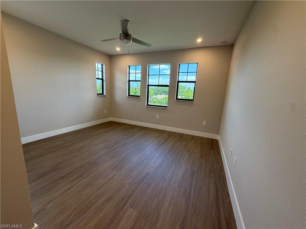 This room features three windows, wood-style flooring, a ceiling fan, and recessed lighting