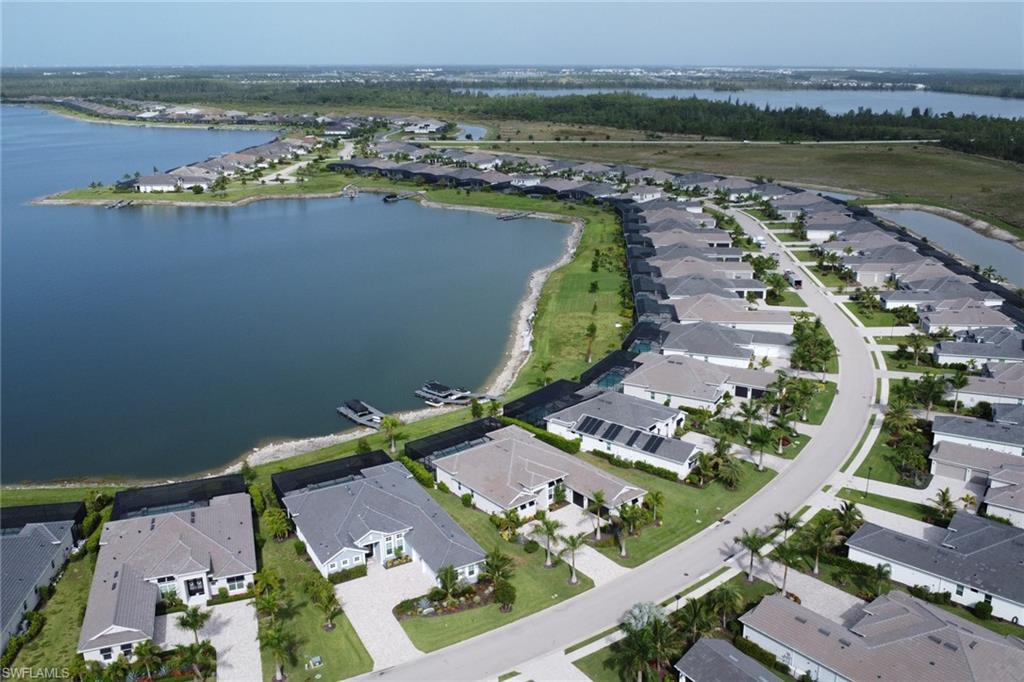 Aerial perspective of a lakeside residential community featuring a curved street, uniform home designs, and verdant landscaping