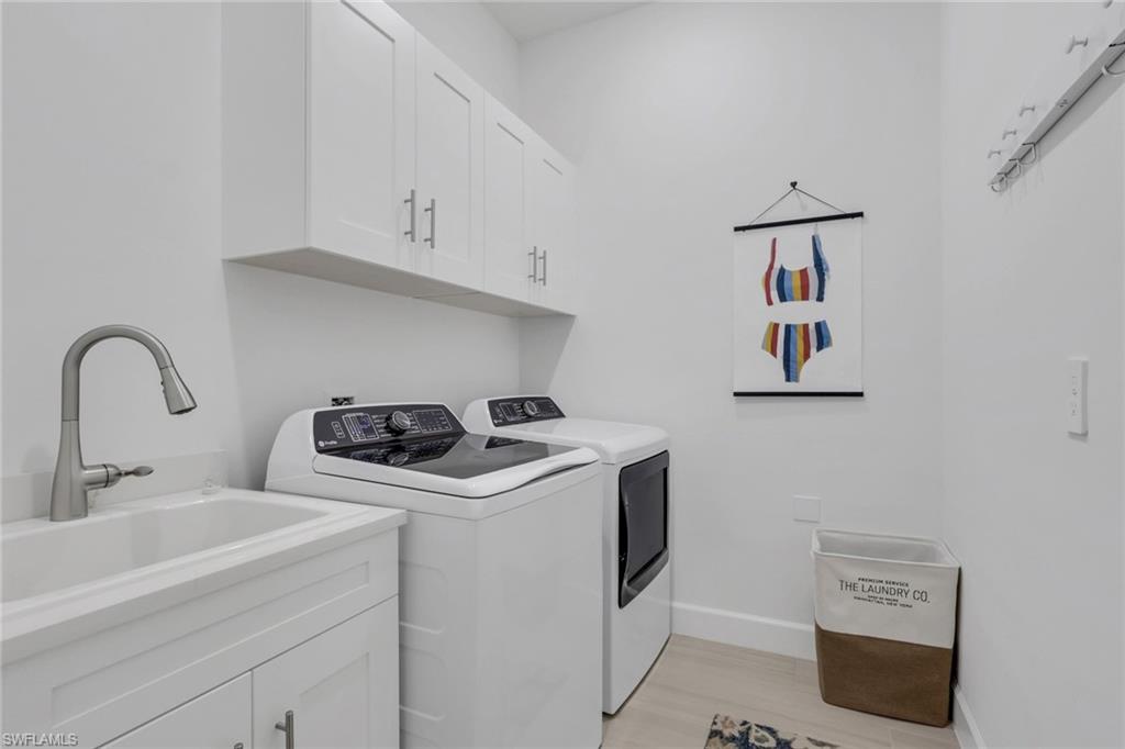 Laundry area featuring white cabinetry, a utility sink with a brushed nickel faucet, light-toned flooring, and wall-mounted coat hooks