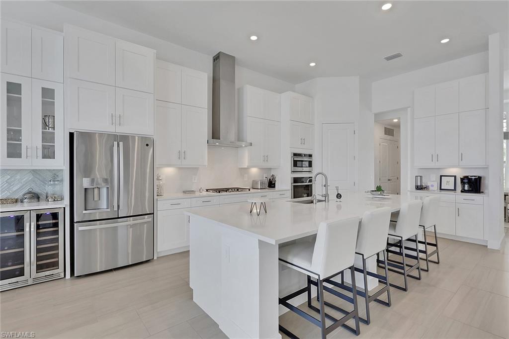 Spacious kitchen featuring white cabinetry, stainless steel appliances, a large center island with seating, recessed lighting, and light wood-finish flooring