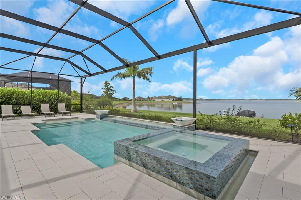 Screened-in outdoor living space featuring a pool and integrated spa with mosaic tile surround, spacious paver patio, and mature landscaping
