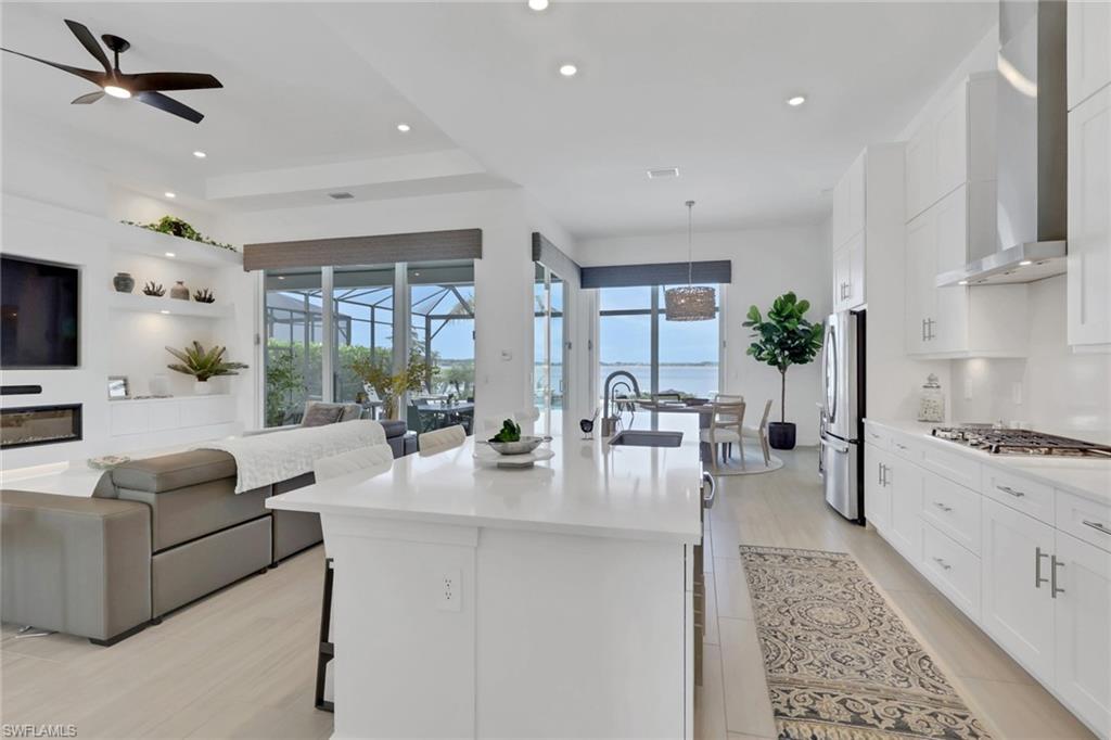 Open-concept living space featuring a modern kitchen with white cabinetry and stainless steel appliances, a center island with a sink, light wood-finish flooring, and recessed lighting
