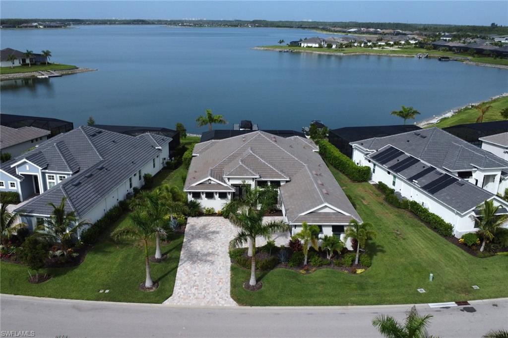 Waterfront property featuring a paver driveway, mature palm trees, tile roofing, and manicured landscaping