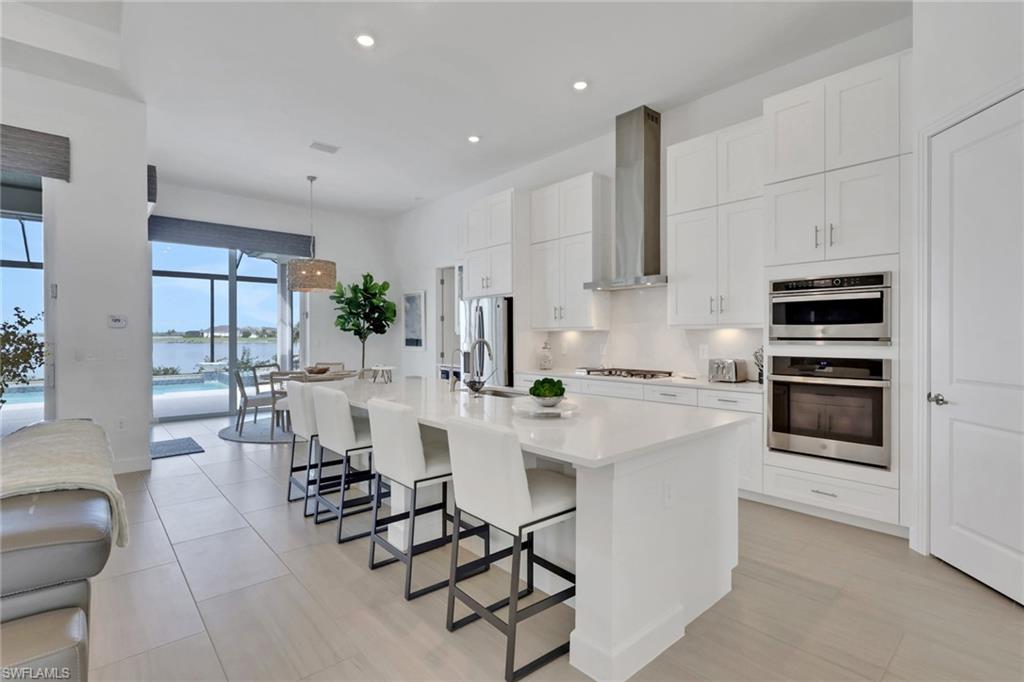 Modern open-concept kitchen featuring a large island with seating, stainless steel appliances, white cabinetry, and light-colored tile flooring