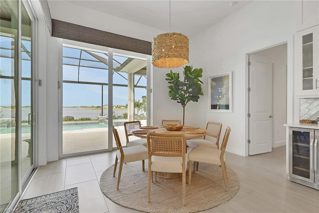 Dining area featuring expansive sliding glass doors, water body scenery, an outdoor screened enclosure, a built-in beverage cooler, and large format tile flooring