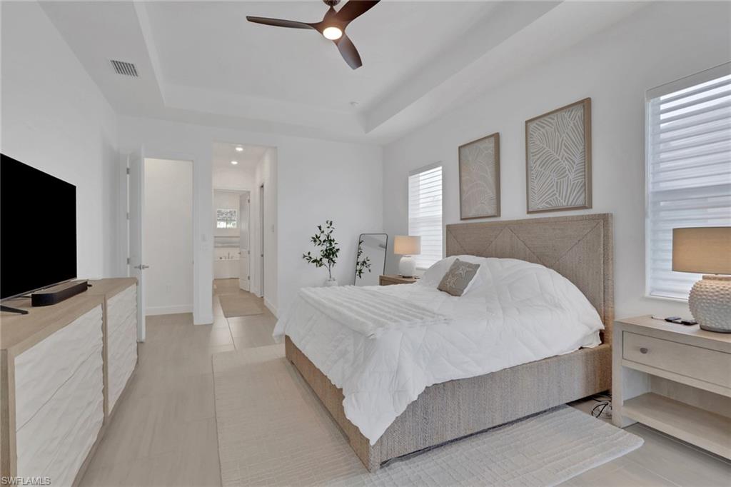 Tray ceiling with a ceiling fan, light wood-finish flooring, and white walls