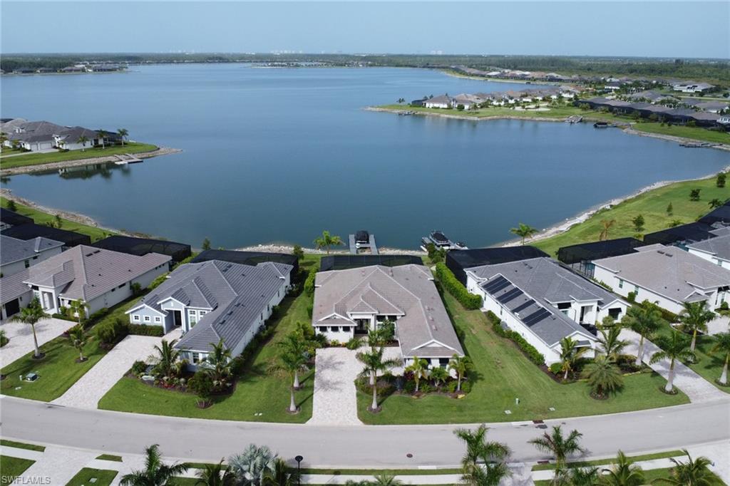 Lakeside property featuring a boat dock, concrete paver driveway, manicured lawn, and mature palm trees