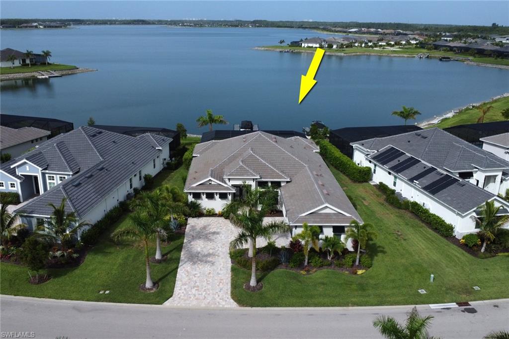 Waterfront property featuring a paver driveway, mature palm trees, tile roof, and manicured lawn
