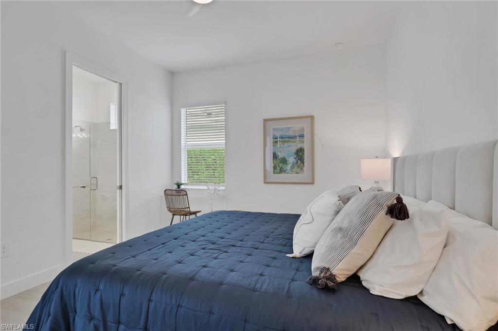 Bedroom featuring a built-in upholstered headboard, a window with horizontal blinds, and a door frame providing access to a glass-enclosed shower