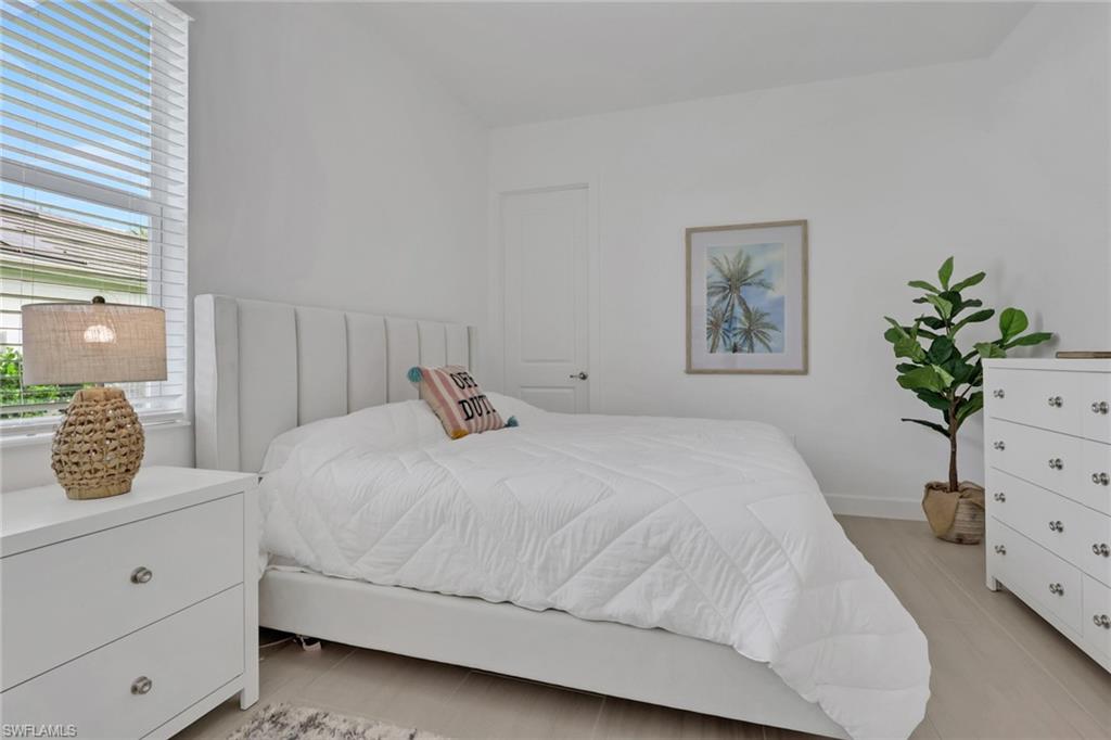 White-painted interior room featuring light wood-finish flooring, a window with horizontal blinds, a white door, and a framed art piece