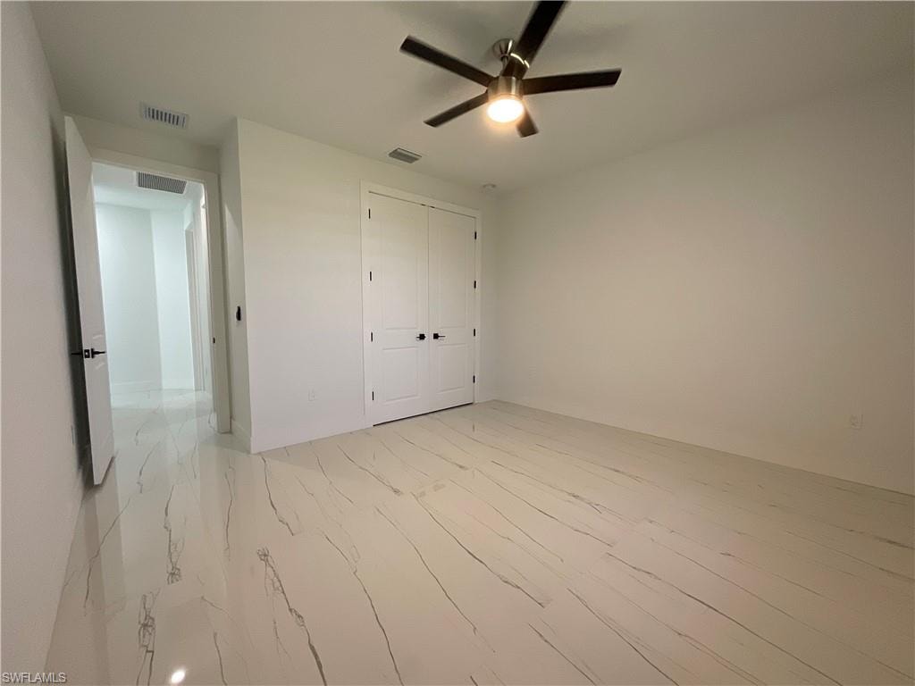 This room features white walls, white tile flooring with dark veining, a white door with a black handle, and a ceiling fan with integrated lighting