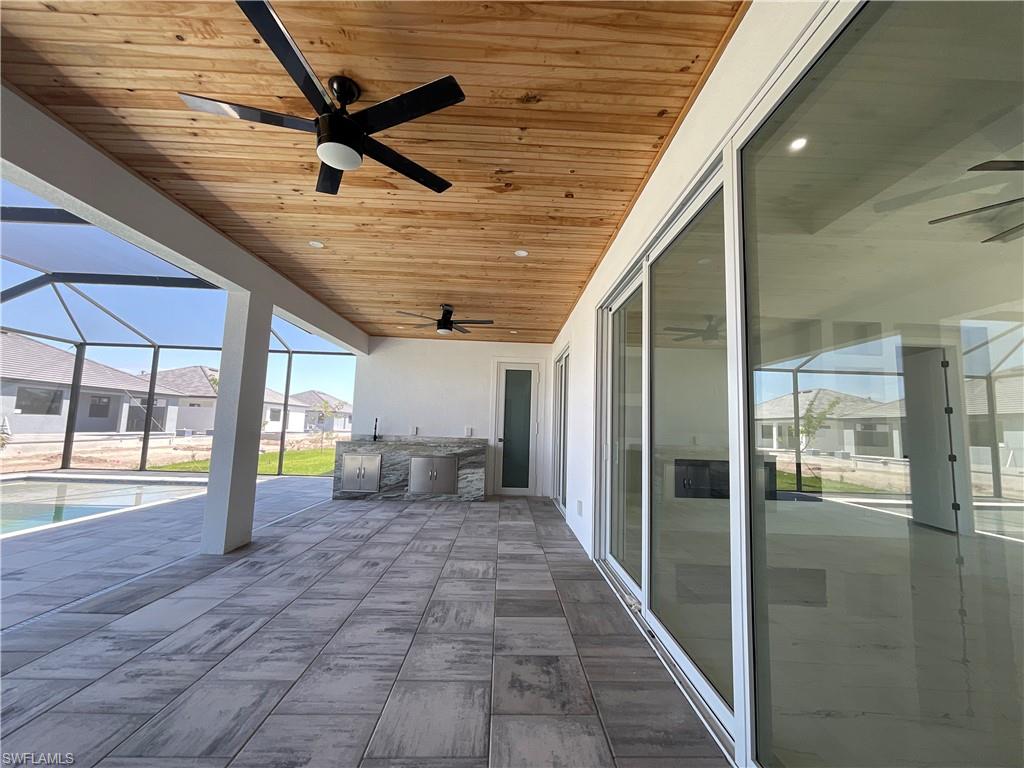 Expansive covered patio featuring a wood plank ceiling, two ceiling fans, and an outdoor kitchen area with a countertop and built-in appliances