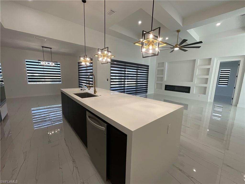 Spacious open-concept living area featuring a large kitchen island with a sink and dishwasher, white tile flooring, and modern lighting fixtures