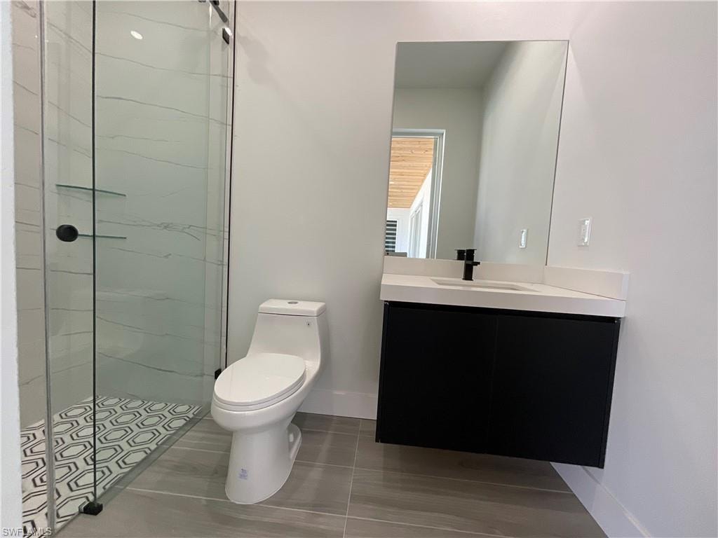 Bathroom featuring a glass-enclosed shower with patterned floor tiles, a modern floating vanity with a white countertop, and a large wall-mounted mirror
