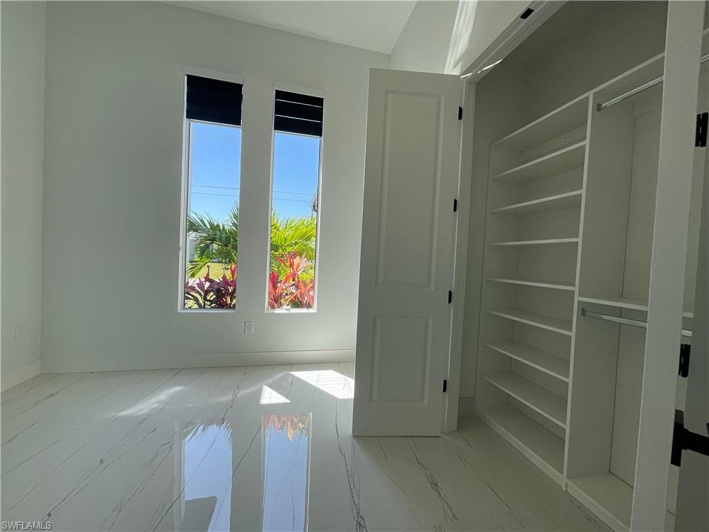 This room features polished flooring, a built-in closet with shelving and hanging rods, and two tall windows providing natural light