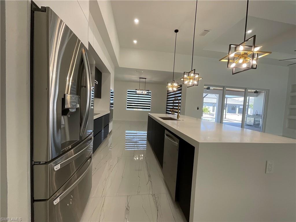 The kitchen features a stainless steel refrigerator, an expansive kitchen island with a built-in sink and dishwasher, and modern pendant lighting