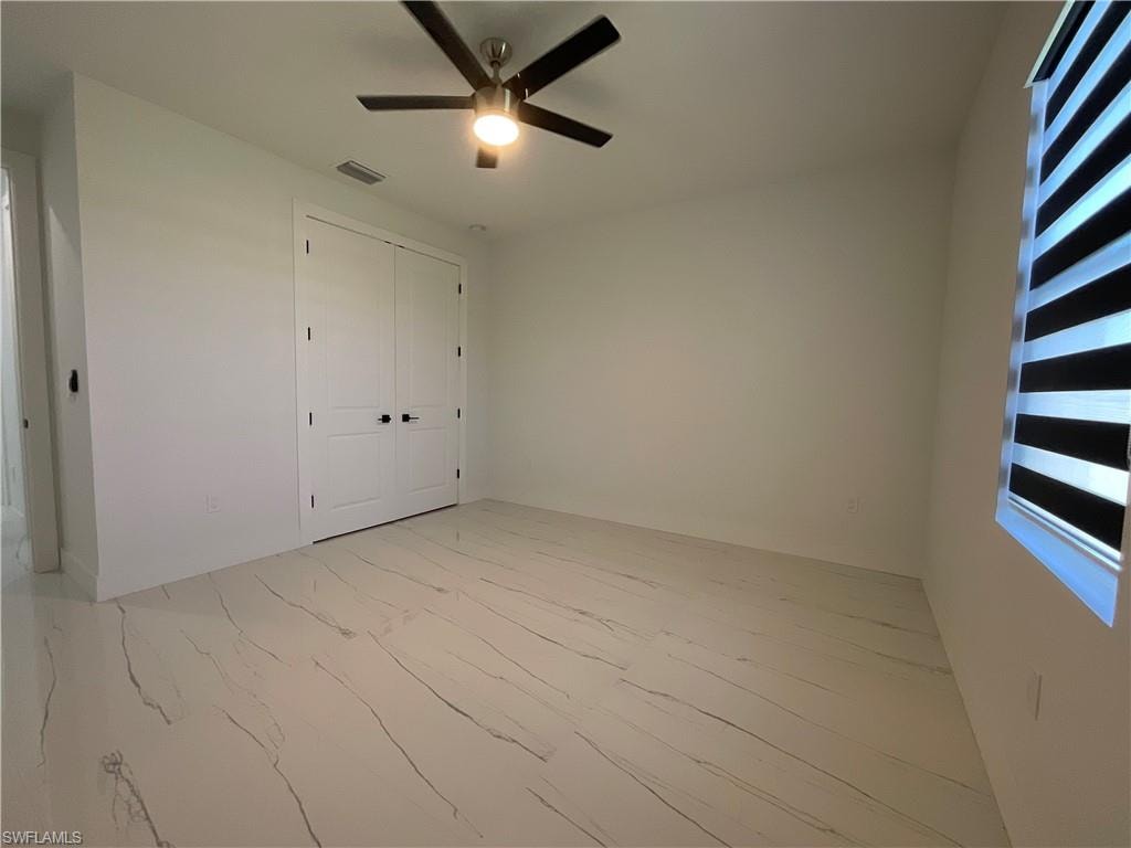 This room features clean white walls, a ceiling fan with integrated lighting, and a large window with horizontal blinds