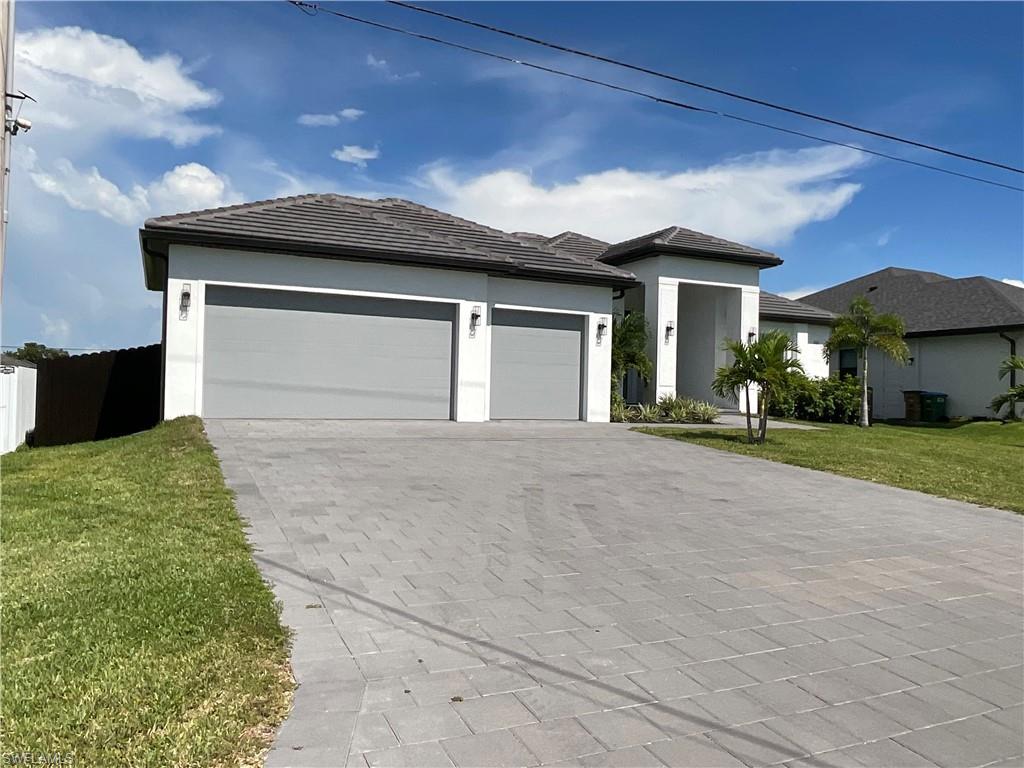 Contemporary stucco exterior, tile roof, dual garage doors, paved driveway, and established landscaping