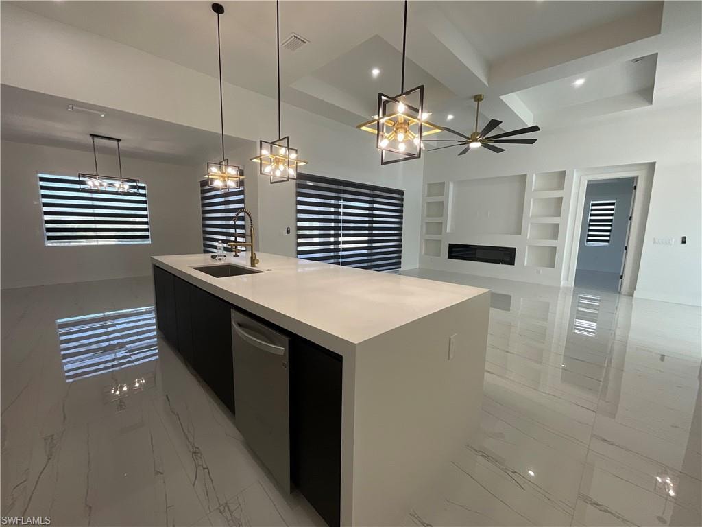 Bright open-concept living space with sleek tile flooring, a spacious kitchen island featuring a sink and dishwasher, and a built-in media center with shelving and a fireplace