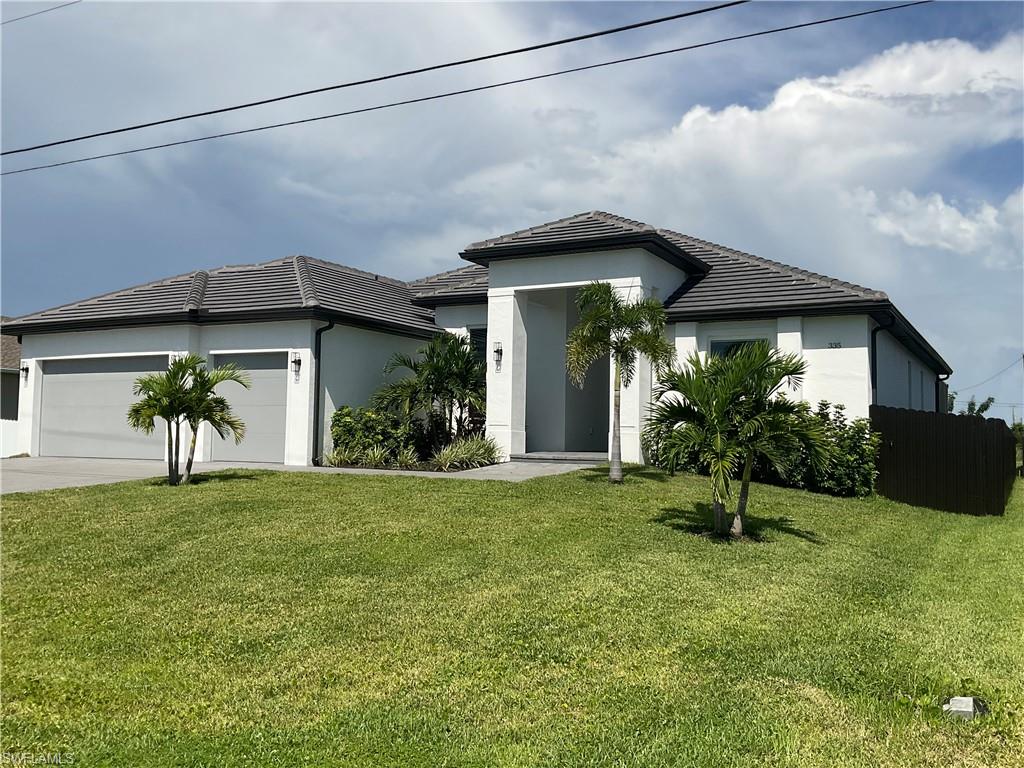 Stucco exterior with a tile roof, two-car garage with gray doors, covered entry, and mature landscaping