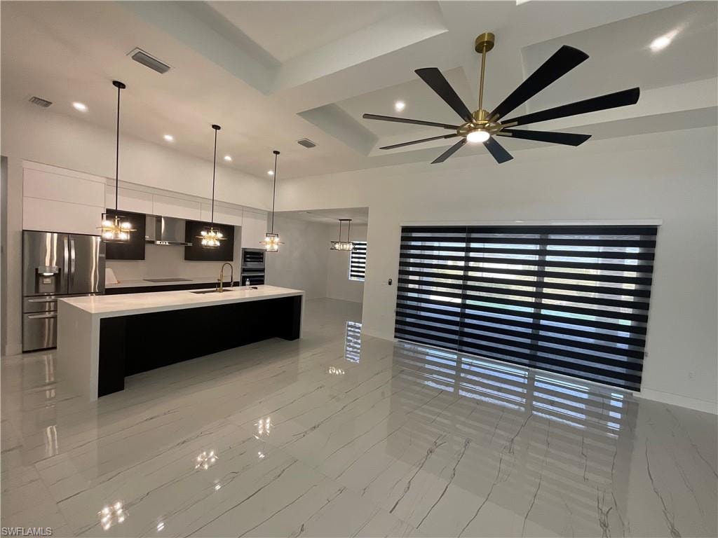 Contemporary kitchen and living area featuring sleek white tile flooring, a large kitchen island with white countertop, stainless steel refrigerator, and recessed lighting
