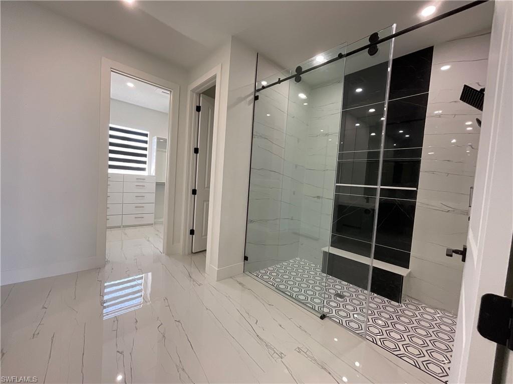 Luxurious bathroom featuring large format tile flooring, a spacious shower with a glass barn door, patterned shower floor tile, and a built-in shower bench