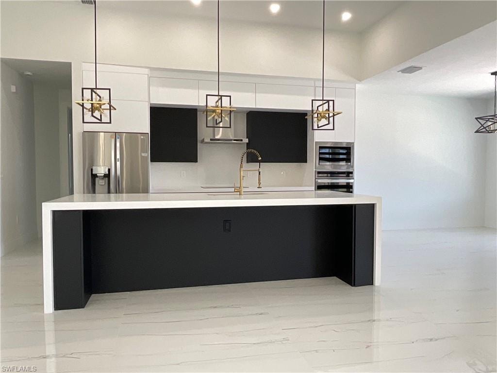 Modern kitchen featuring a large island with a white countertop and dark cabinetry, stainless steel appliances, and sleek pendant lighting fixtures