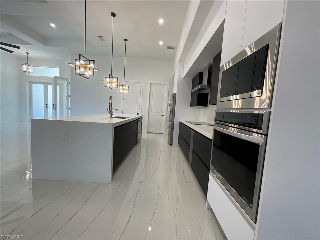 The kitchen features a large island with a sink and modern pendant lighting, sleek white and black cabinetry, built-in stainless steel appliances, and polished tile flooring