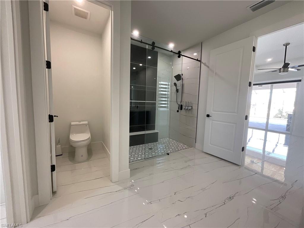 This bathroom features large format white tile flooring with grey veining, a glass-enclosed shower with a tiled bench and a distinct patterned floor, and a separate toilet area