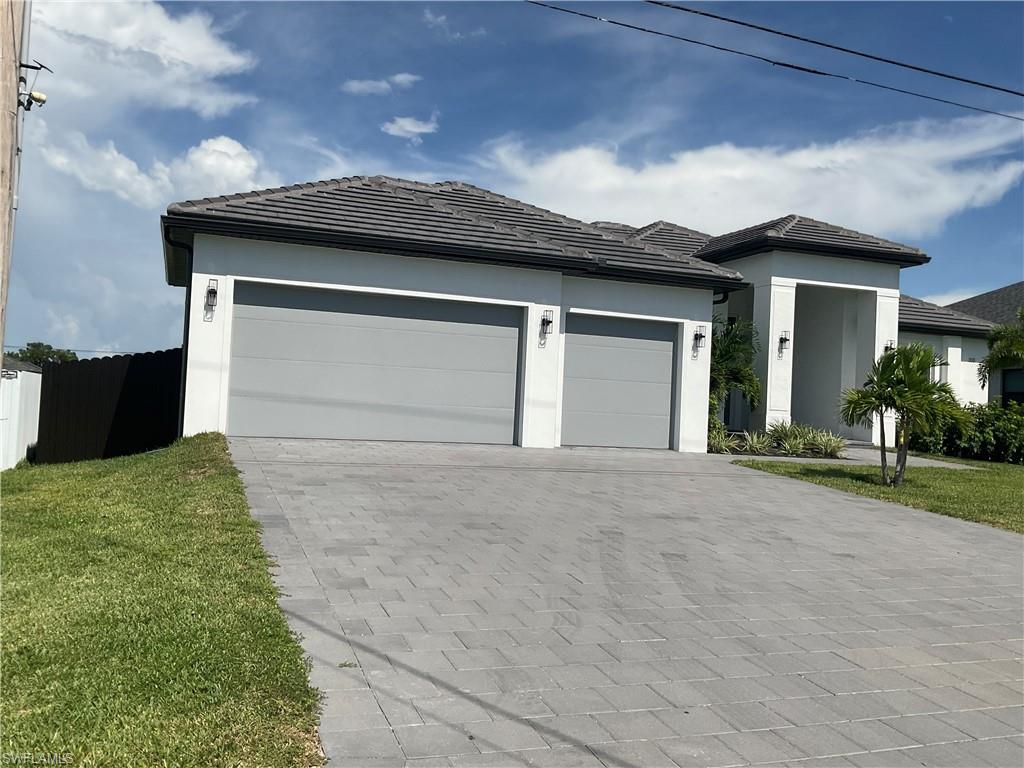 Stucco exterior with a tiled roof, paver driveway, two garage doors, and exterior wall sconces