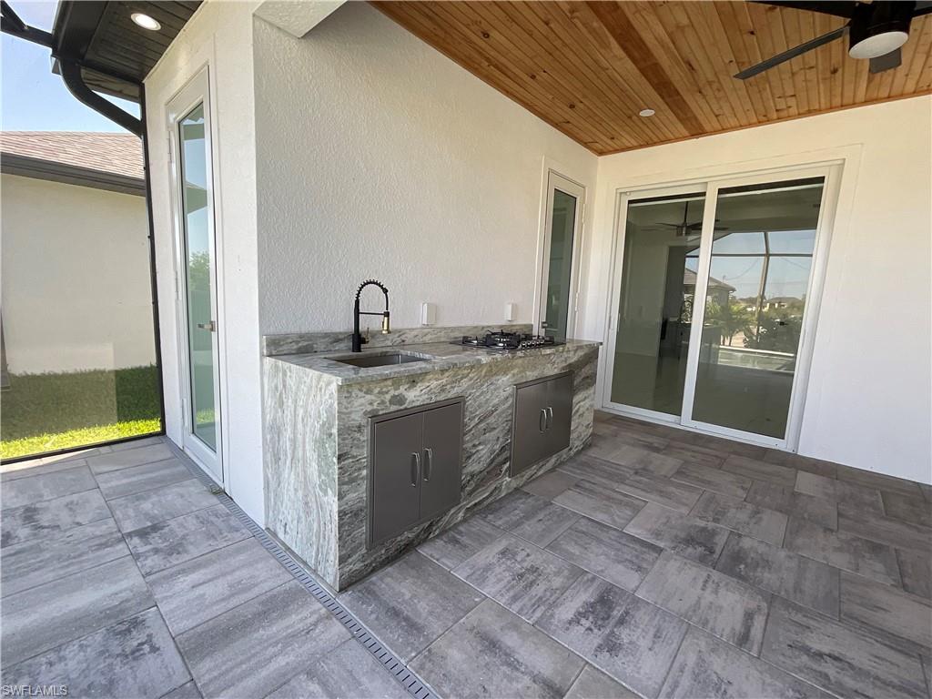The property features an outdoor kitchen with a stone countertop, an integrated sink with a black faucet, and built-in storage cabinets