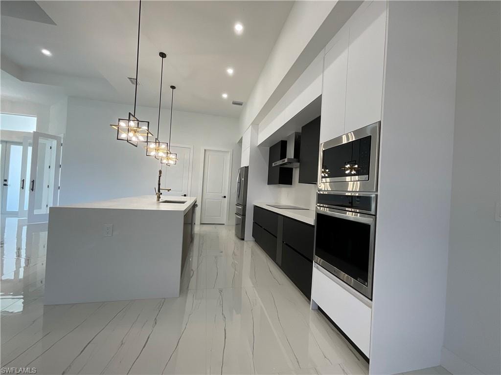 Modern kitchen featuring an expansive island with a sink, recessed lighting, and stylish pendant light fixtures