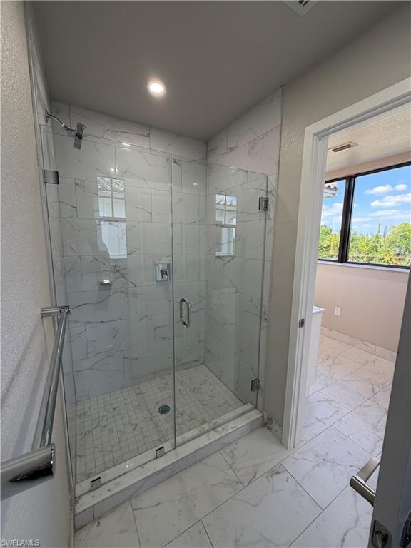 The bathroom features a spacious glass-enclosed shower with white marble-style tiled walls and a tiled floor