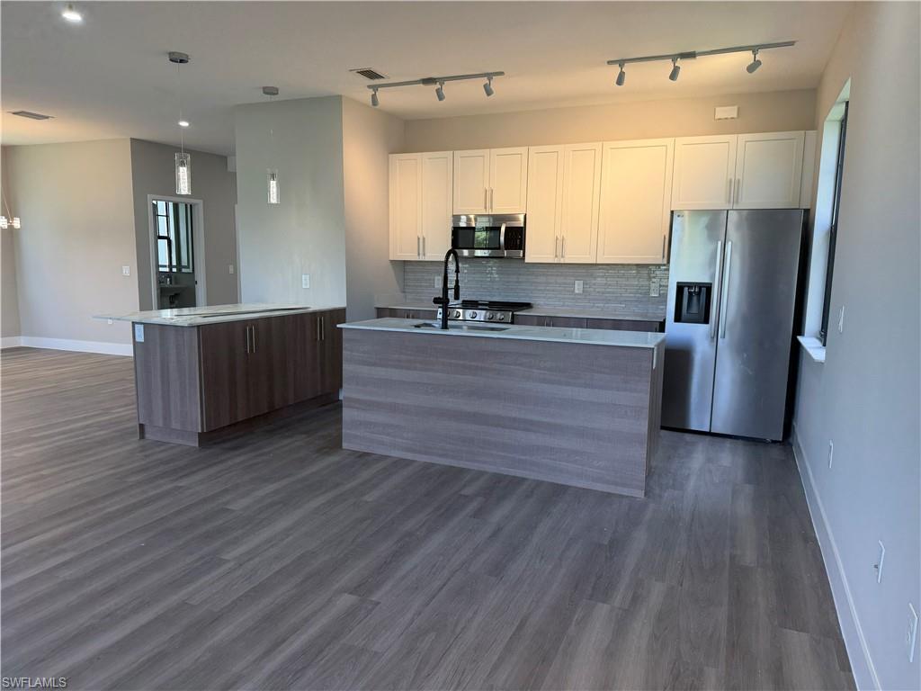 Contemporary kitchen featuring two islands, white cabinetry, stainless steel appliances, and track lighting