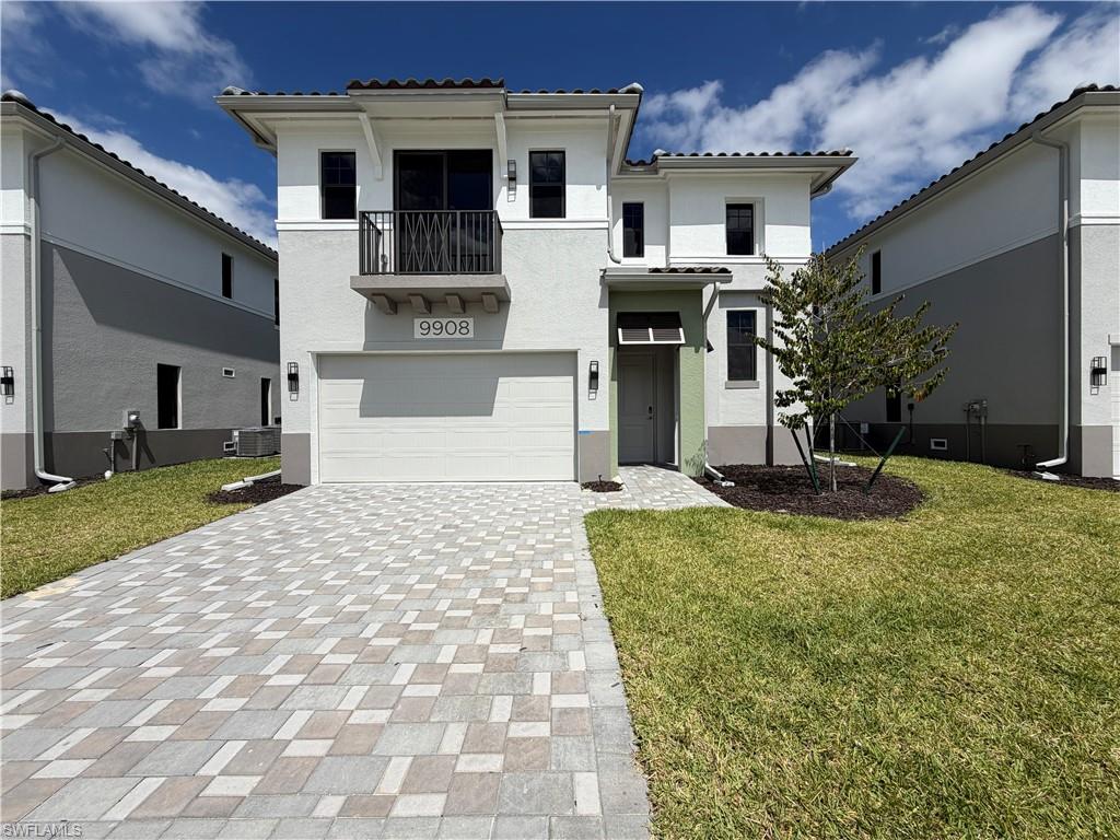 The property features a paver driveway, an attached garage, and a balcony with a black railing