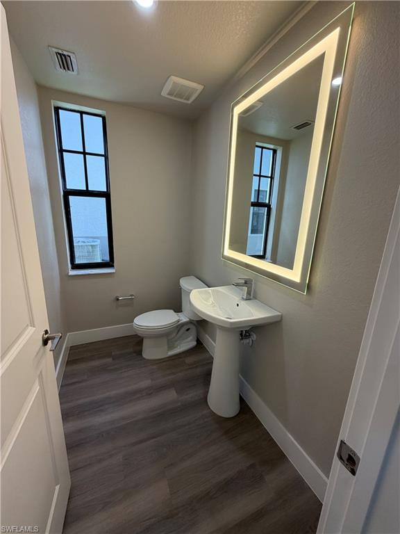 This powder room features wood-look flooring, a pedestal sink with a chrome faucet, and a contemporary mirror with integrated lighting