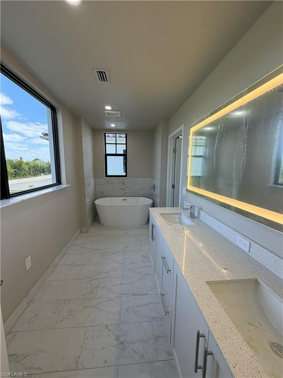 Well-appointed bathroom featuring a freestanding bathtub, a double vanity with quartz countertops, and a large illuminated mirror